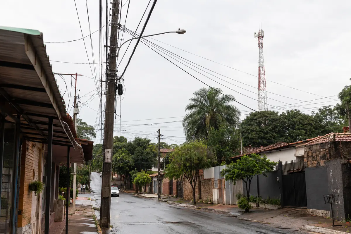 Cableado de telecomunicaciones y una antena celular en una calle residencial de Asunción después de la lluvia