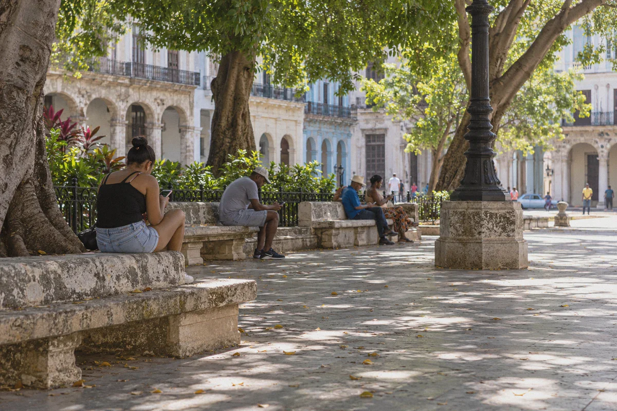 People using phones in a shaded Havana public square.