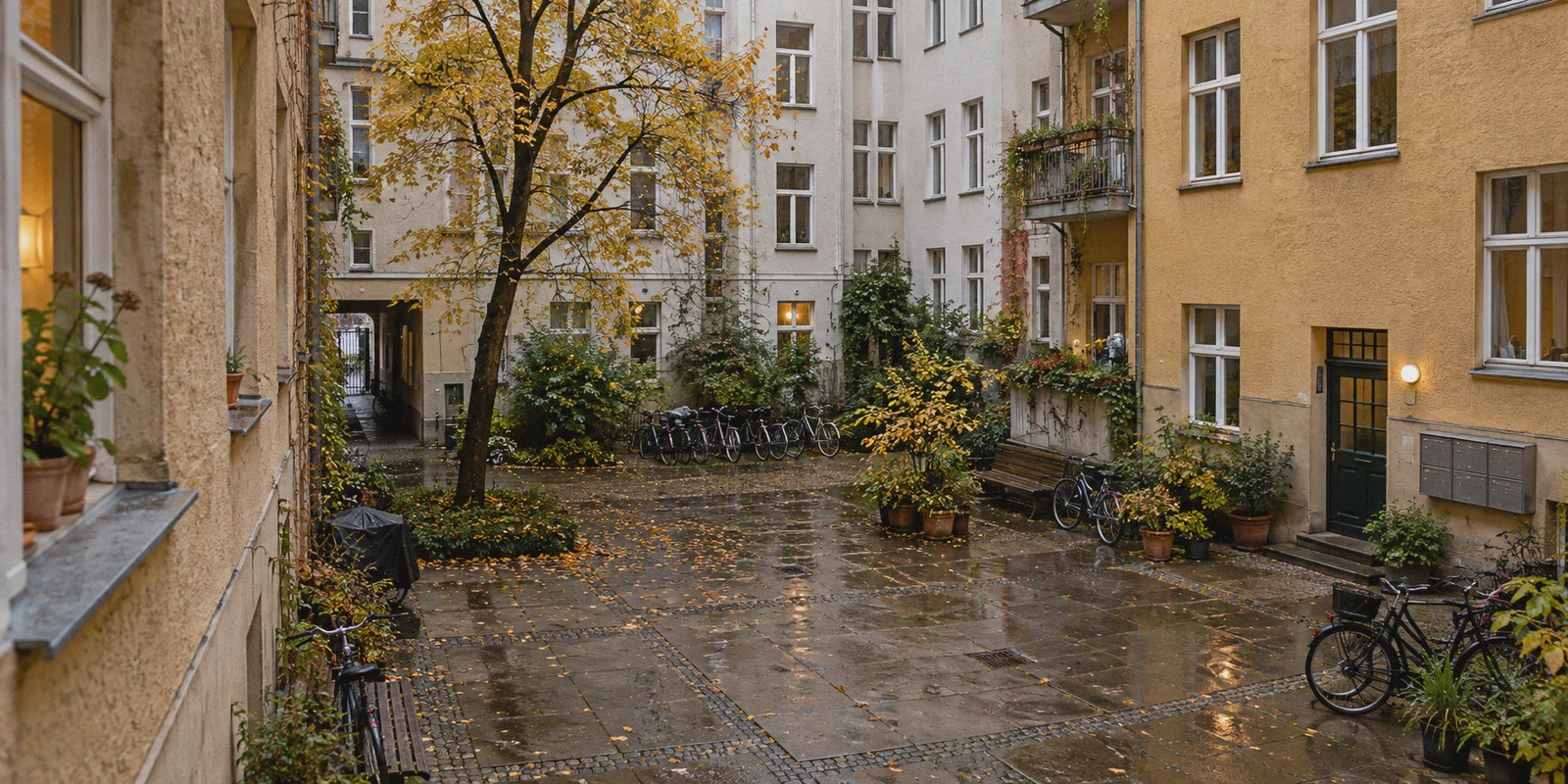 A quiet Berlin residential courtyard seen from a shared-flat window, stucco apartment facades, bicycles and mailboxes, damp paving, overcast autumn morning
