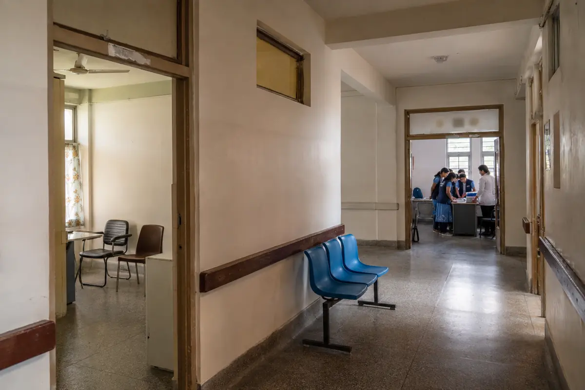 An empty hospital room near a corridor leading to volunteers coordinating in another room