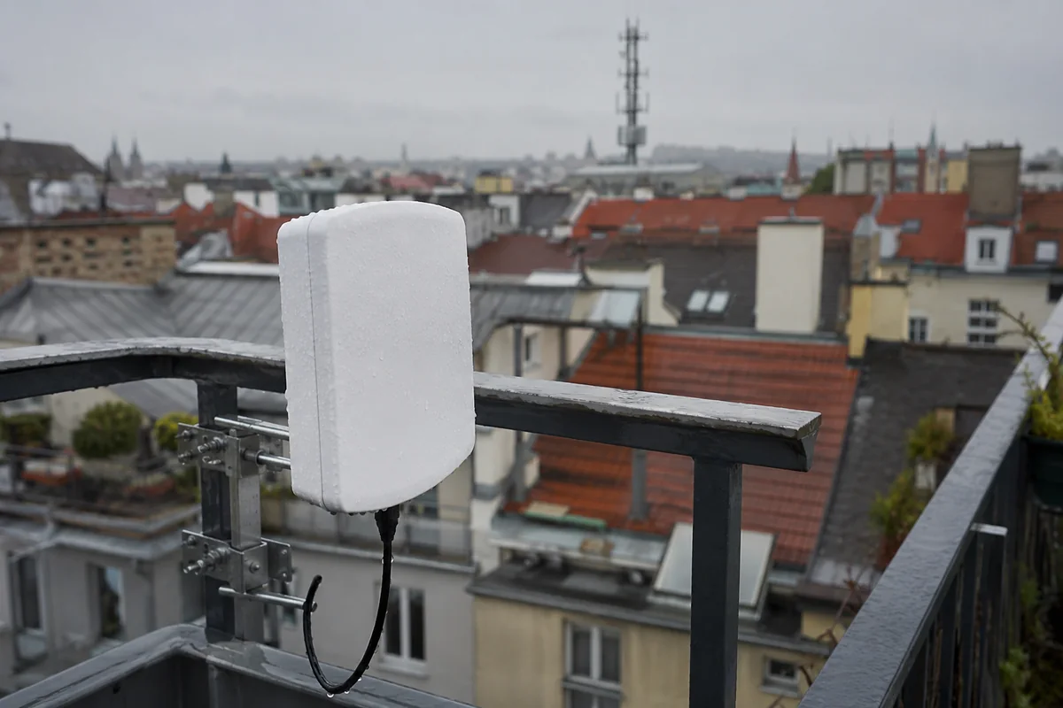 Nasser 5G-Außenempfänger auf einem Wiener Balkon mit Mobilfunkmast im Hintergrund