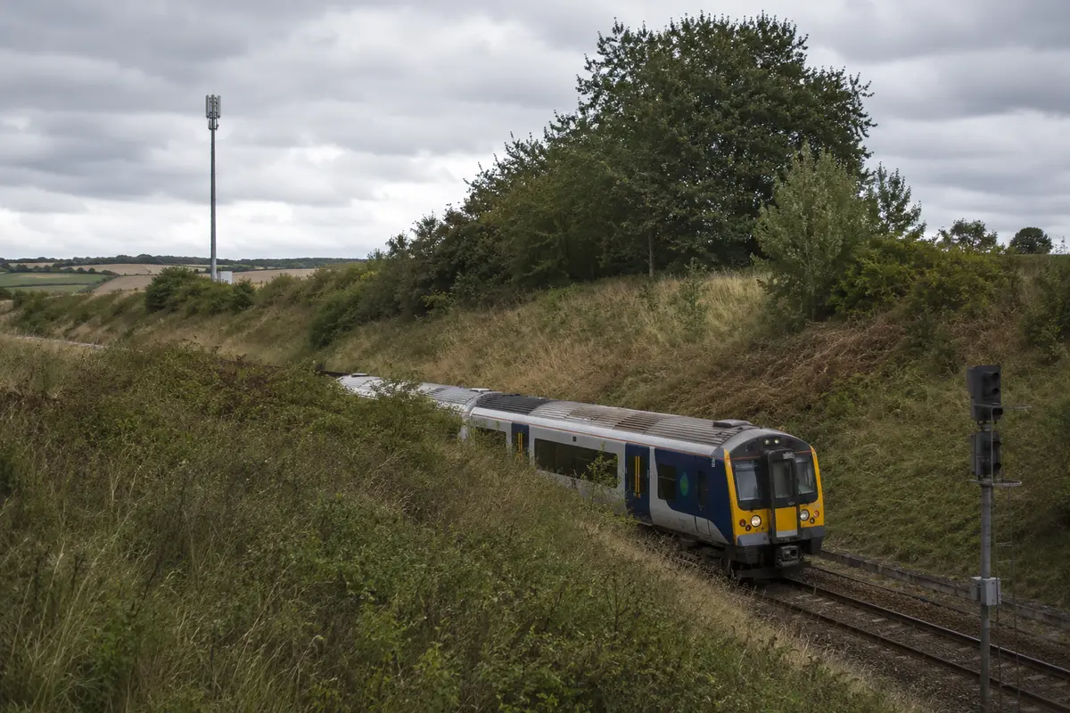 Ein britischer Zug fährt durch einen Geländeeinschnitt neben einem Mobilfunkmast