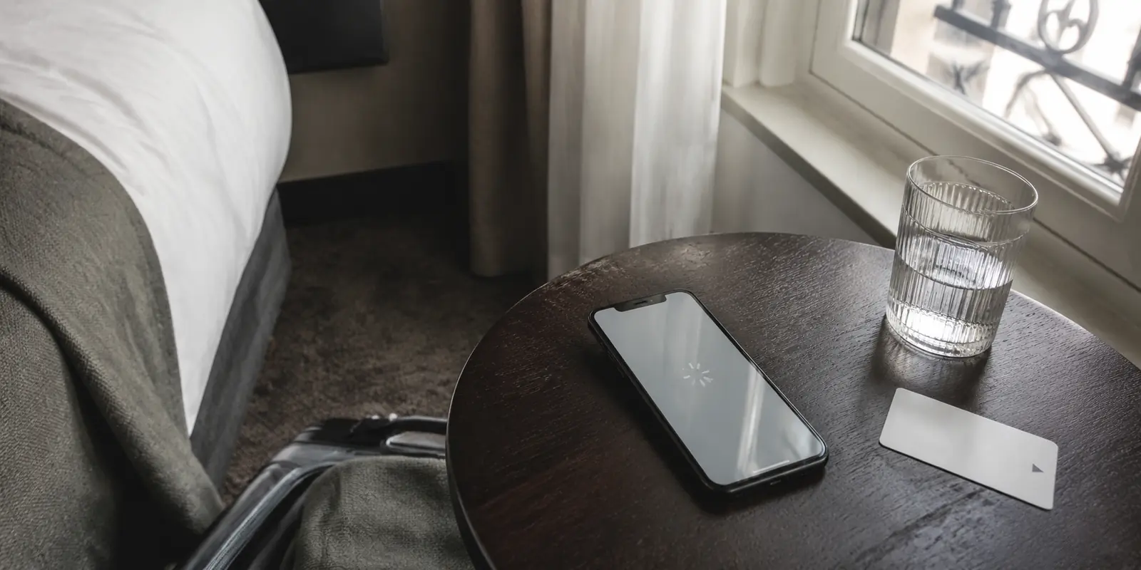 Ein iPhone mit ladendem Bildschirm liegt im Hotelzimmer neben Schlüsselkarte und Reisegepäck