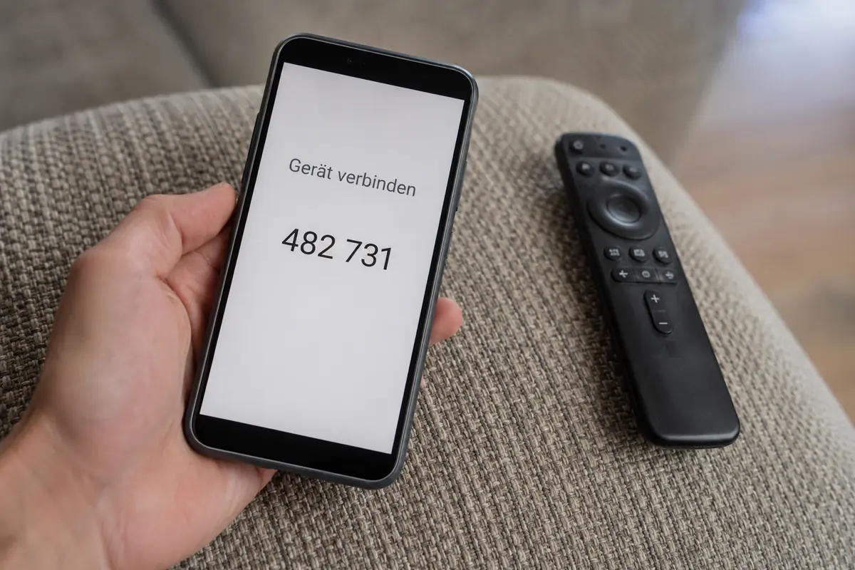 Ein Smartphone zeigt einen kurzen Verbindungscode neben einer unbenutzten TV-Fernbedienung