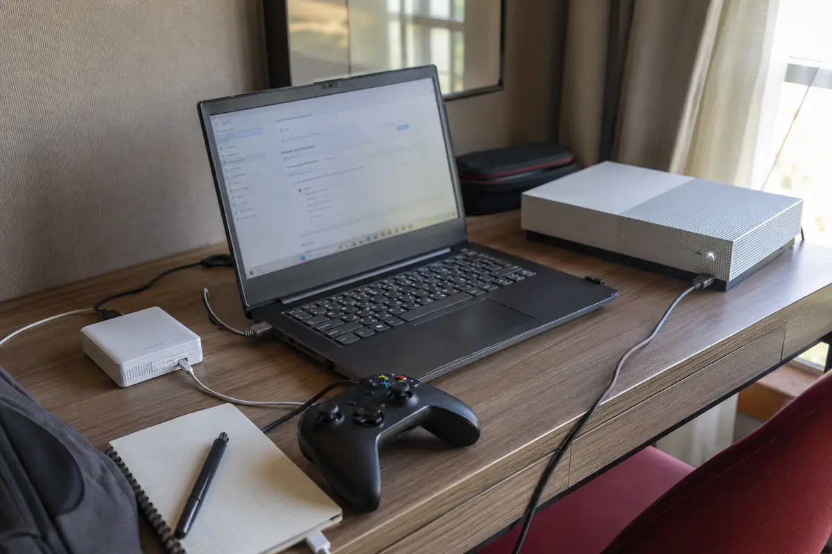 Laptop teilt im Hotel seine Verbindung mit einer Spielkonsole, während der Travel-Router danebensteht