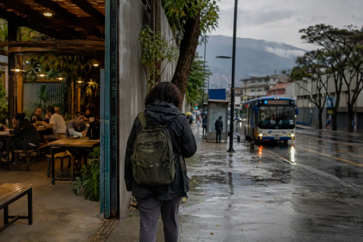 Trabajador remoto saliendo de un café hacia una parada de autobús bajo la lluvia en San José, Costa Rica