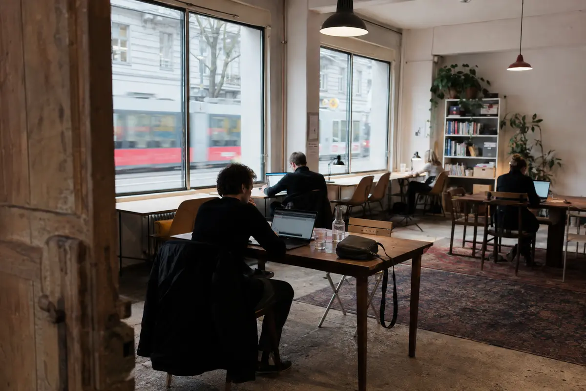Remote-Arbeitende in einem Wiener Coworking-Space mit vorbeifahrender Straßenbahn