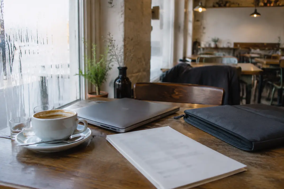 Ein geschlossener Laptop, Unterlagen und eine fast leere Kaffeetasse in einem winterlichen Café