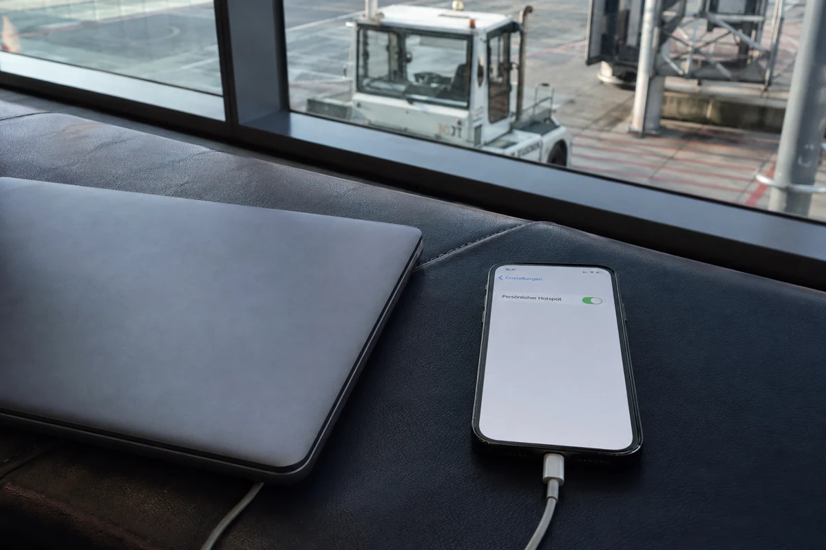 Ein Smartphone mit aktiviertem persönlichen Hotspot liegt neben einem geschlossenen Laptop am Flughafen