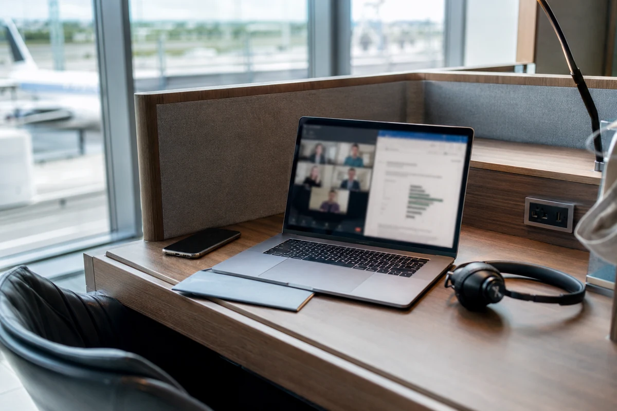 Laptop mit Videocall und Dokument neben Smartphone und Headset in einer Flughafen-Arbeitskabine