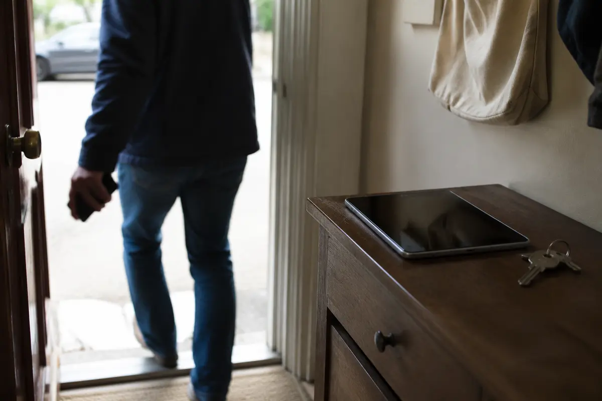Pessoa sai de casa com o telefone enquanto o tablet permanece no móvel de entrada