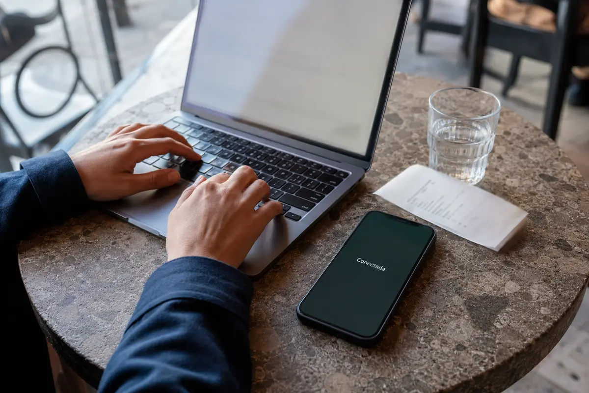 Un portátil y un teléfono conectado se utilizan a la vez en una mesa de cafetería