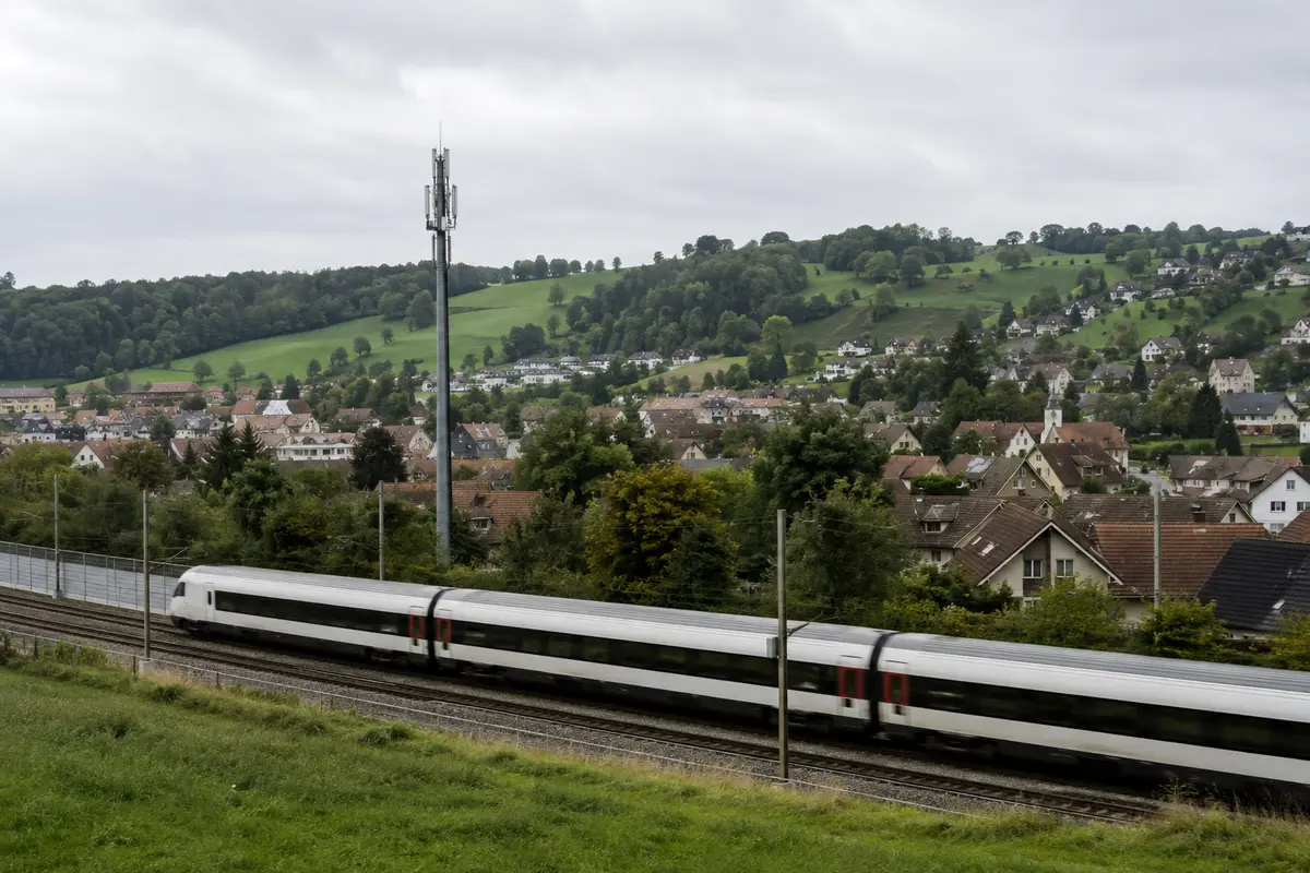 Ein Intercity-Zug fährt durch wechselnde Schweizer Landschaft an einer Mobilfunkantenne vorbei
