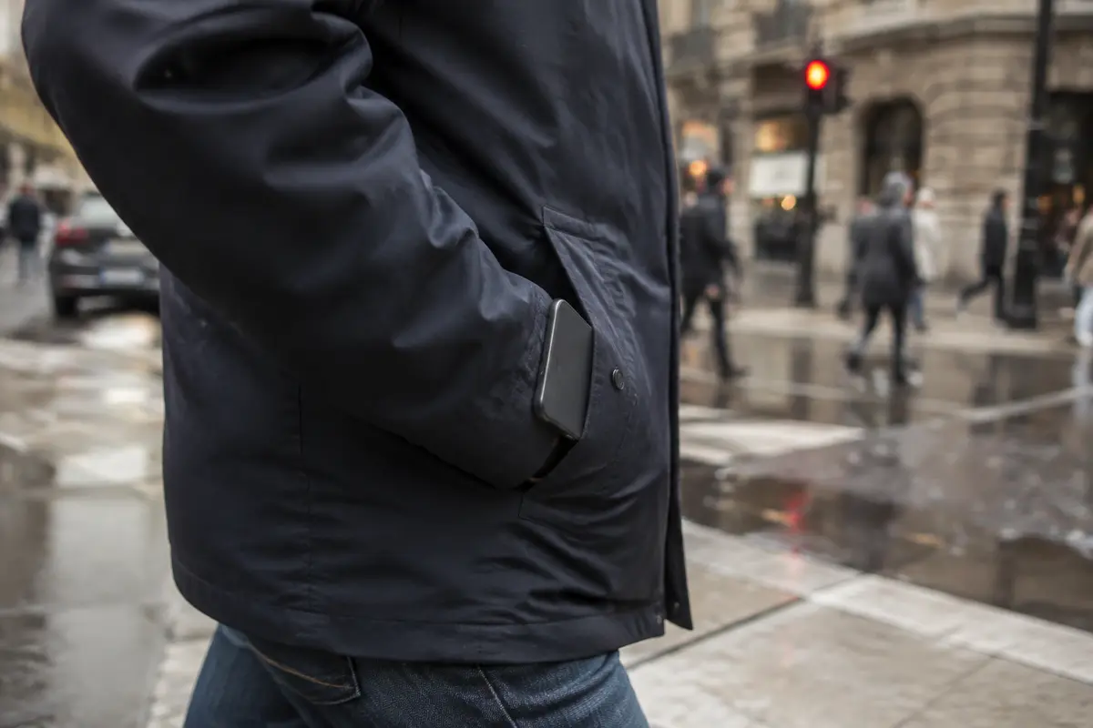 Un teléfono guardado en el bolsillo mientras su dueño cruza una calle mojada