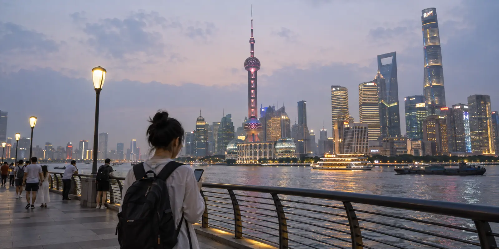 A traveler checks a phone on Shanghai's Bund at dusk