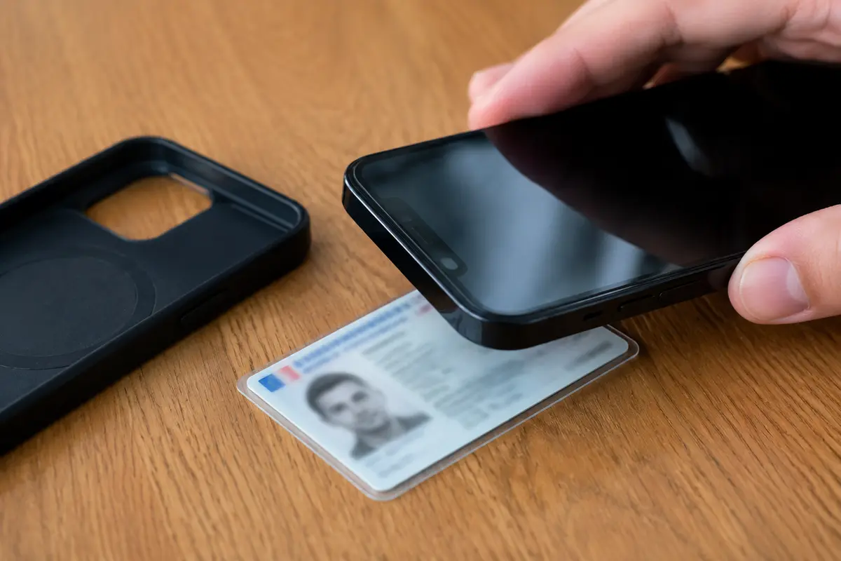 Le haut d’un téléphone maintenu contre une carte d’identité posée à plat, avec la coque retirée
