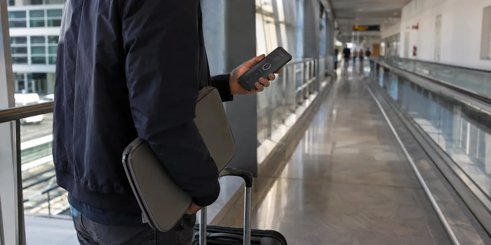 Viajero con portátil cerrado y teléfono en proceso de reconexión mientras cambia de zona en un aeropuerto