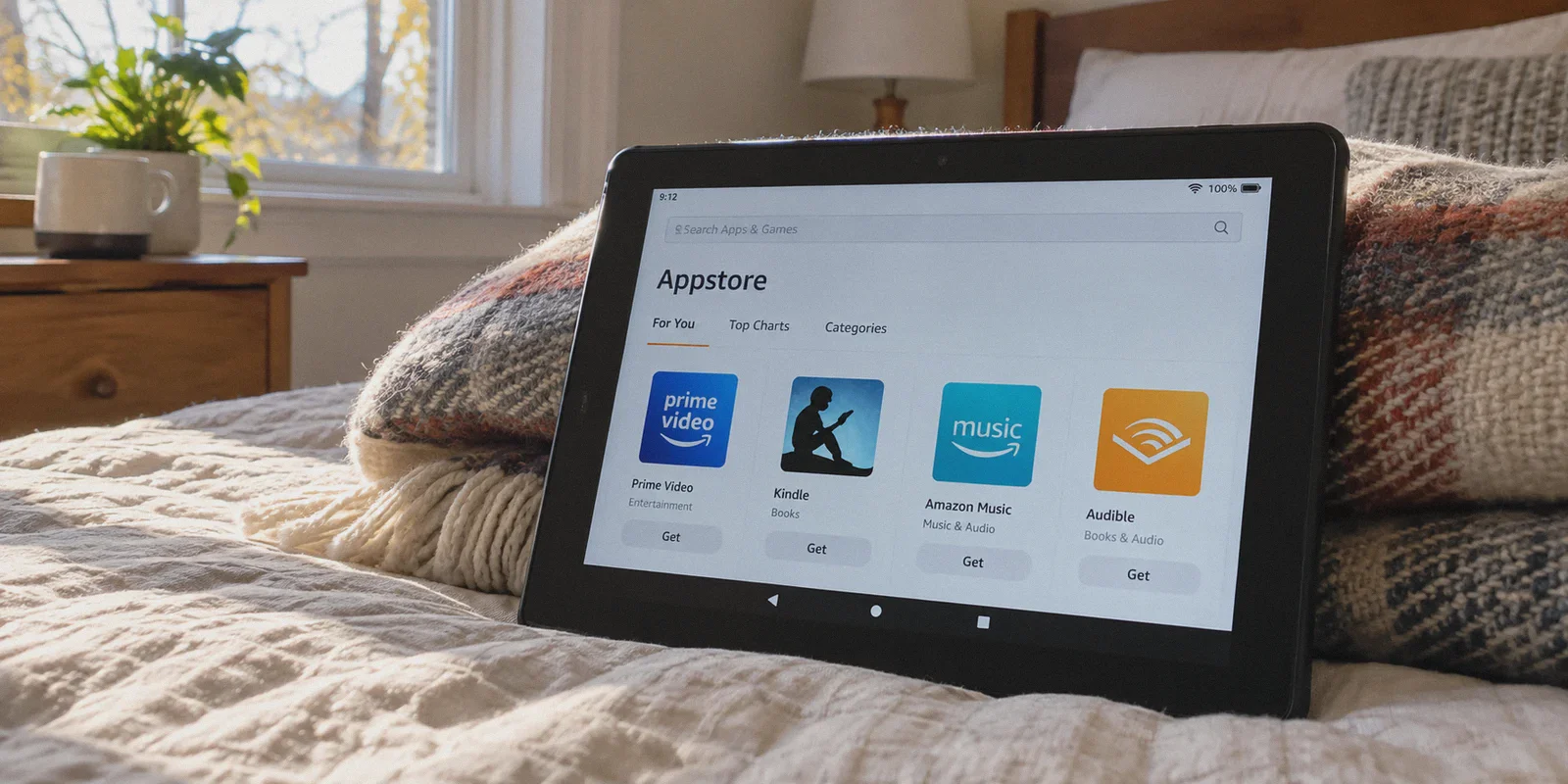 A thick black Amazon Fire tablet propped against a folded wool blanket on a bed.