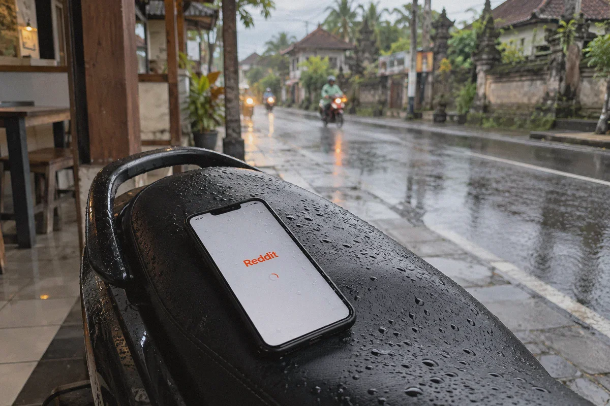 A rain-speckled smartphone on a black scooter seat beneath a roadside shelter in Bali.