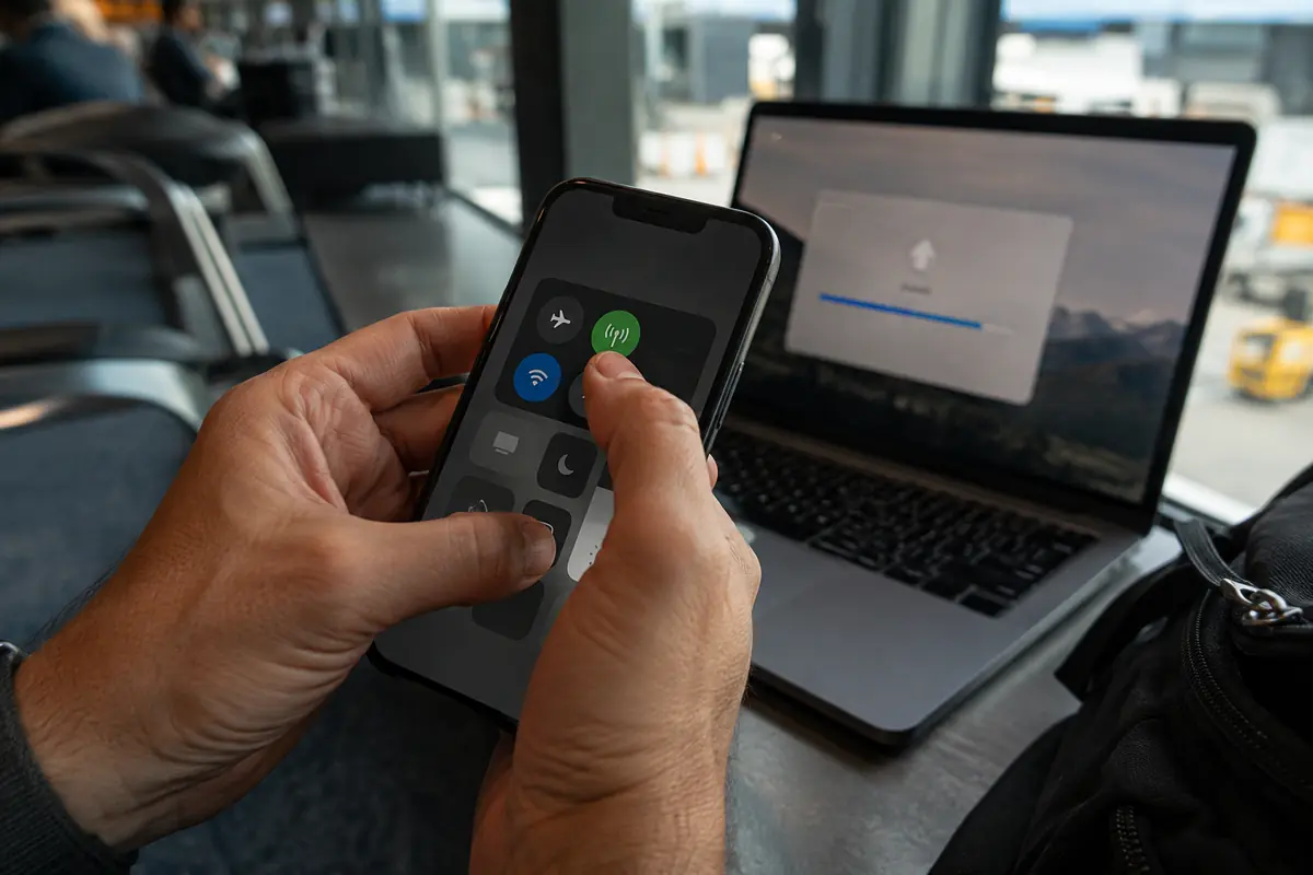 Viajero activa los datos móviles del teléfono mientras una carga continúa en el portátil