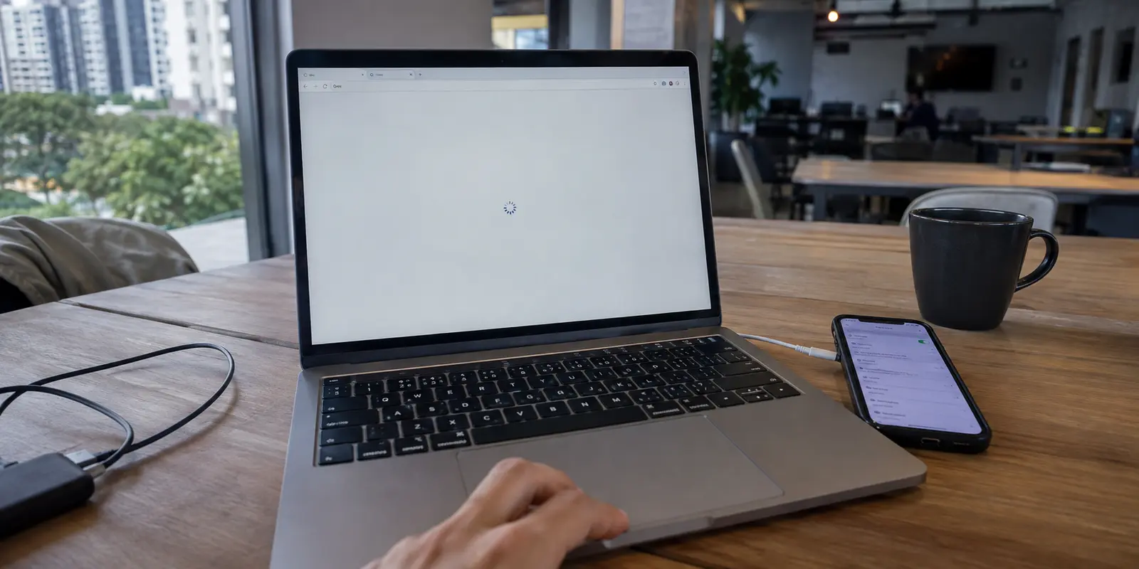 MacBook com uma página presa no carregamento ao lado de um celular usado como hotspot em um coworking