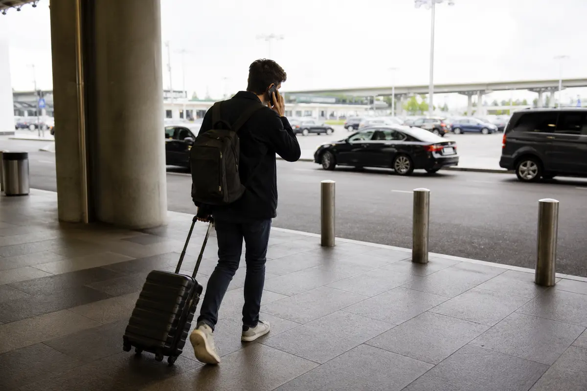 Viajante falando ao celular enquanto sai de um terminal com sua mala