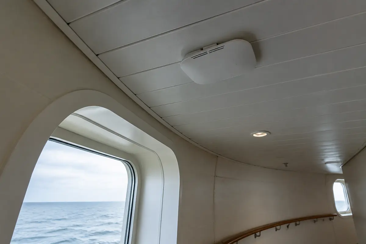 Ponto de acesso Wi-Fi instalado no teto curvo de uma passagem de navio com o mar visível pela janela