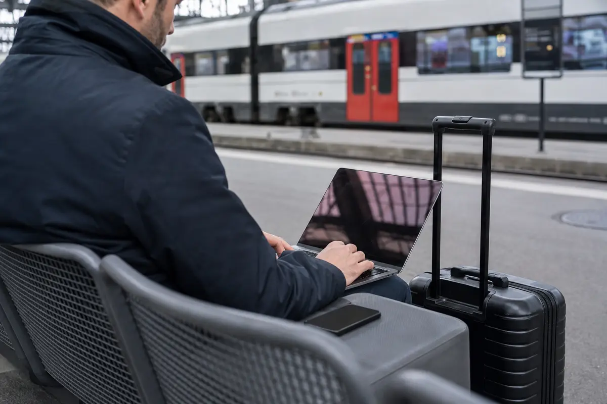 Reisender mit Laptop und Smartphone beim Umsteigen an einem Schweizer Bahnhof