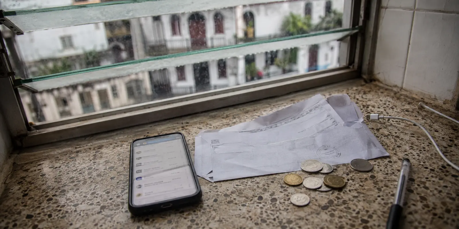 Teléfono, factura abierta y monedas sobre una encimera junto a una ventana lluviosa en Panamá