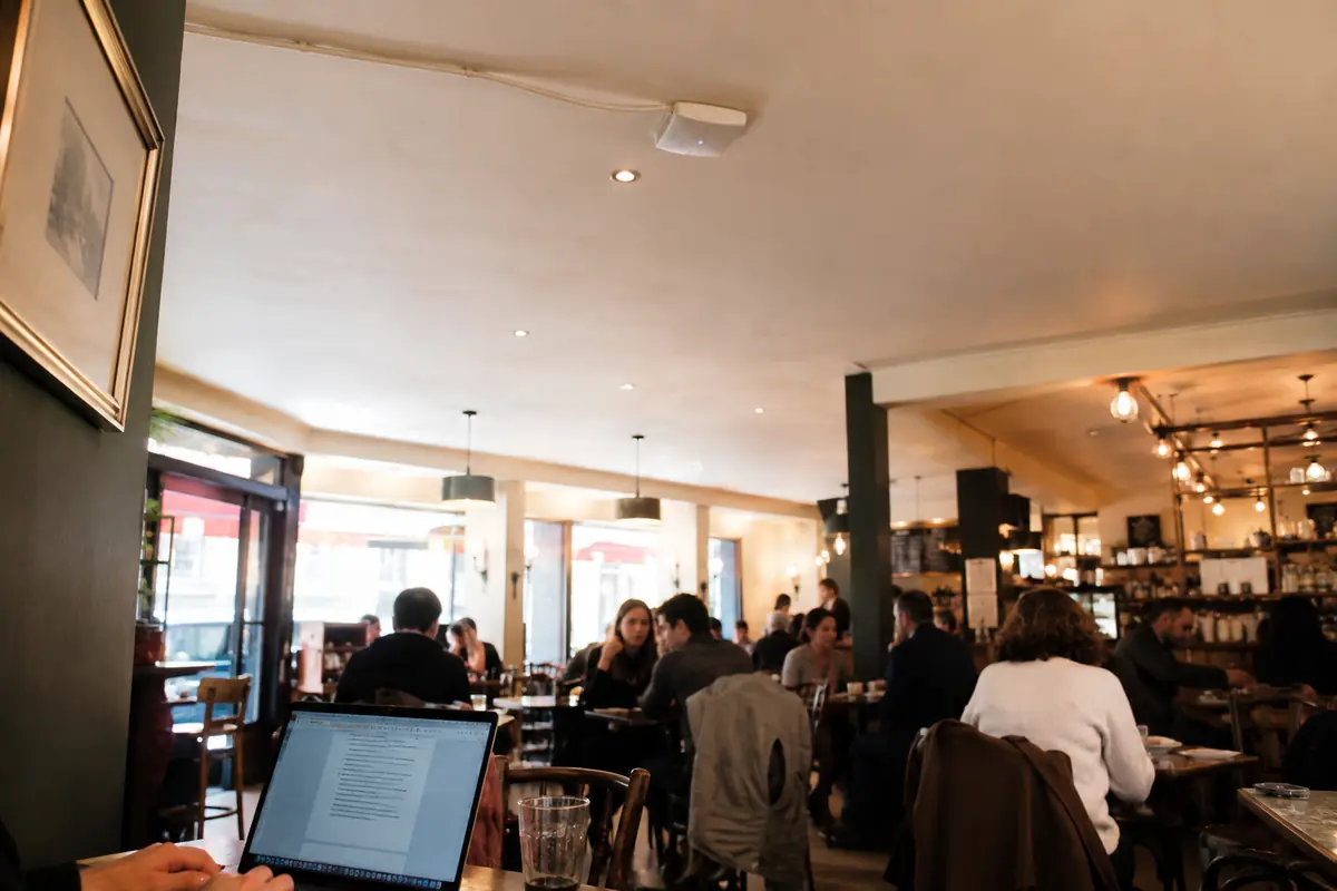 Un point d’accès Wi-Fi au plafond d’un café fréquenté, avec un ordinateur ouvert au premier plan