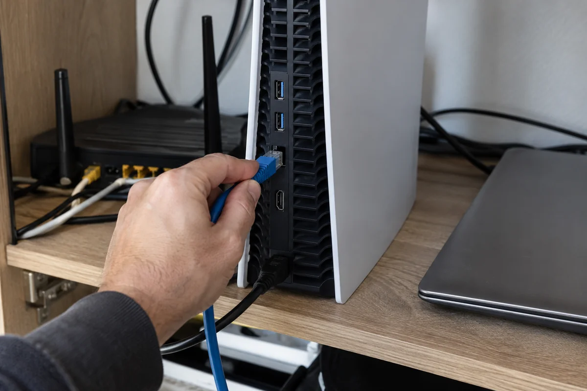 An Ethernet cable being connected directly to a PS5 beside a home router.