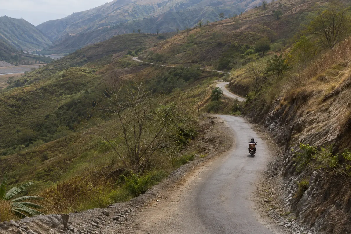 Motociclista segue por uma estrada estreita entre colinas de Timor-Leste