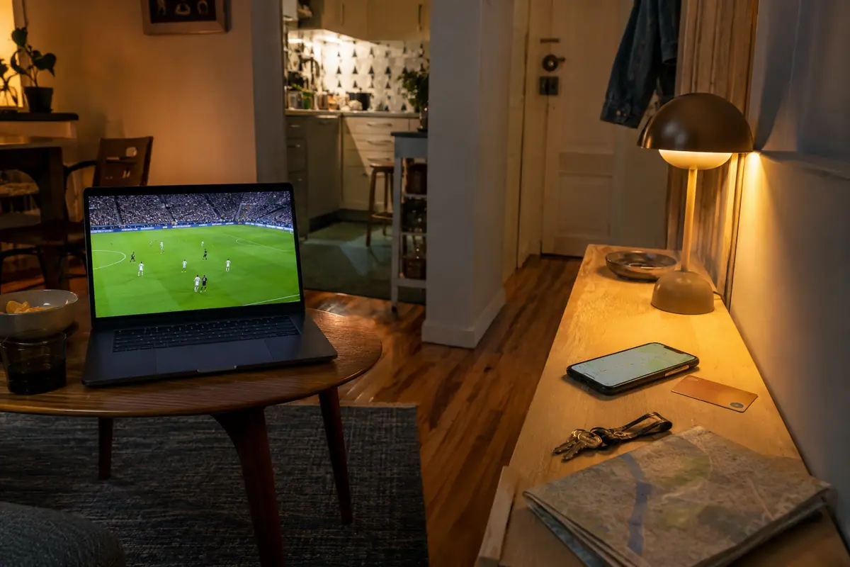 Notebook exibindo futebol em uma mesa e celular separado com mapa local em um aparador de apartamento em Lisboa