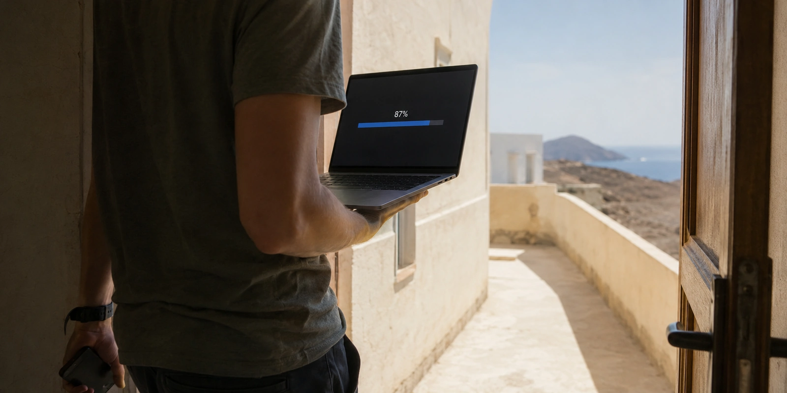 Viajante atravessando a porta do hotel em Cabo Verde com um upload parado em 87% no notebook