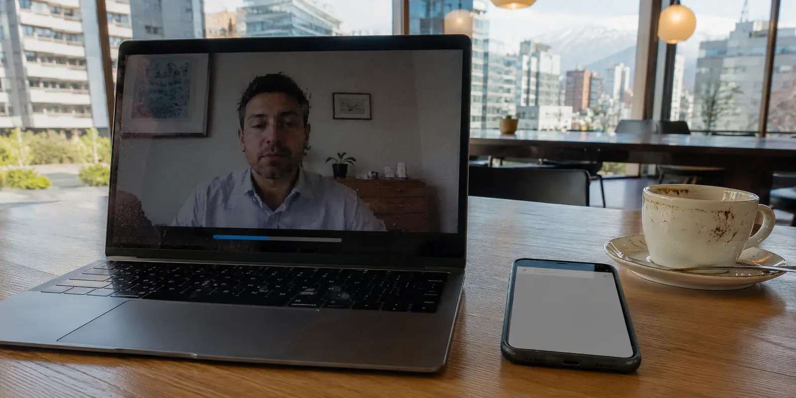 Laptop con videollamada interrumpida y teléfono bancario en una mesa de coworking