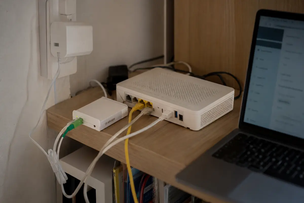 Une installation fibre domestique avec son boîtier, ses câbles réseau et l’interface de la box ouverte sur un ordinateur