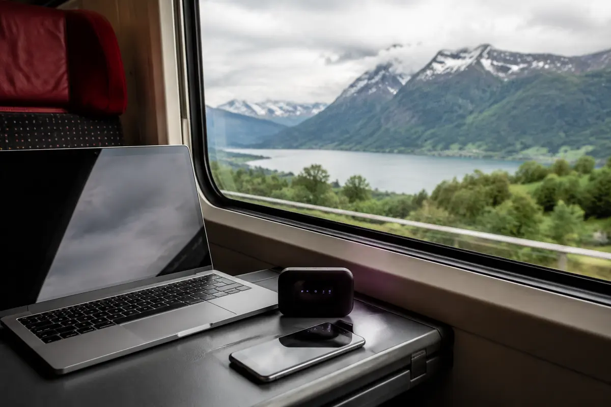 Ordinateur et routeur de voyage devant un paysage suisse vu depuis un train