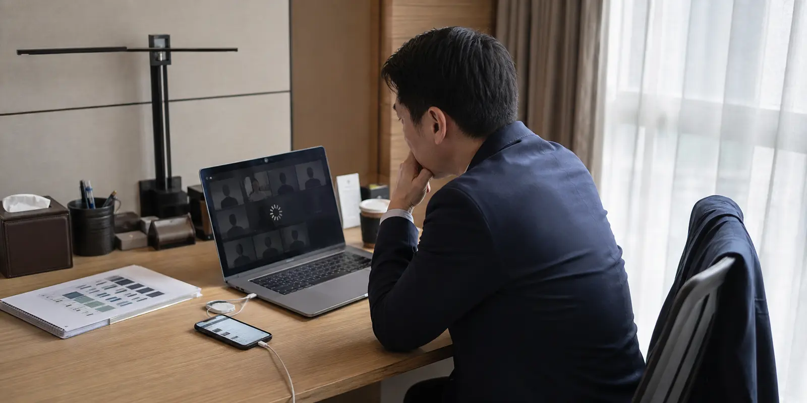 Dans une chambre d’hôtel à Shanghai, un voyageur d’affaires attend devant une visioconférence bloquée tandis que son téléphone reste connecté