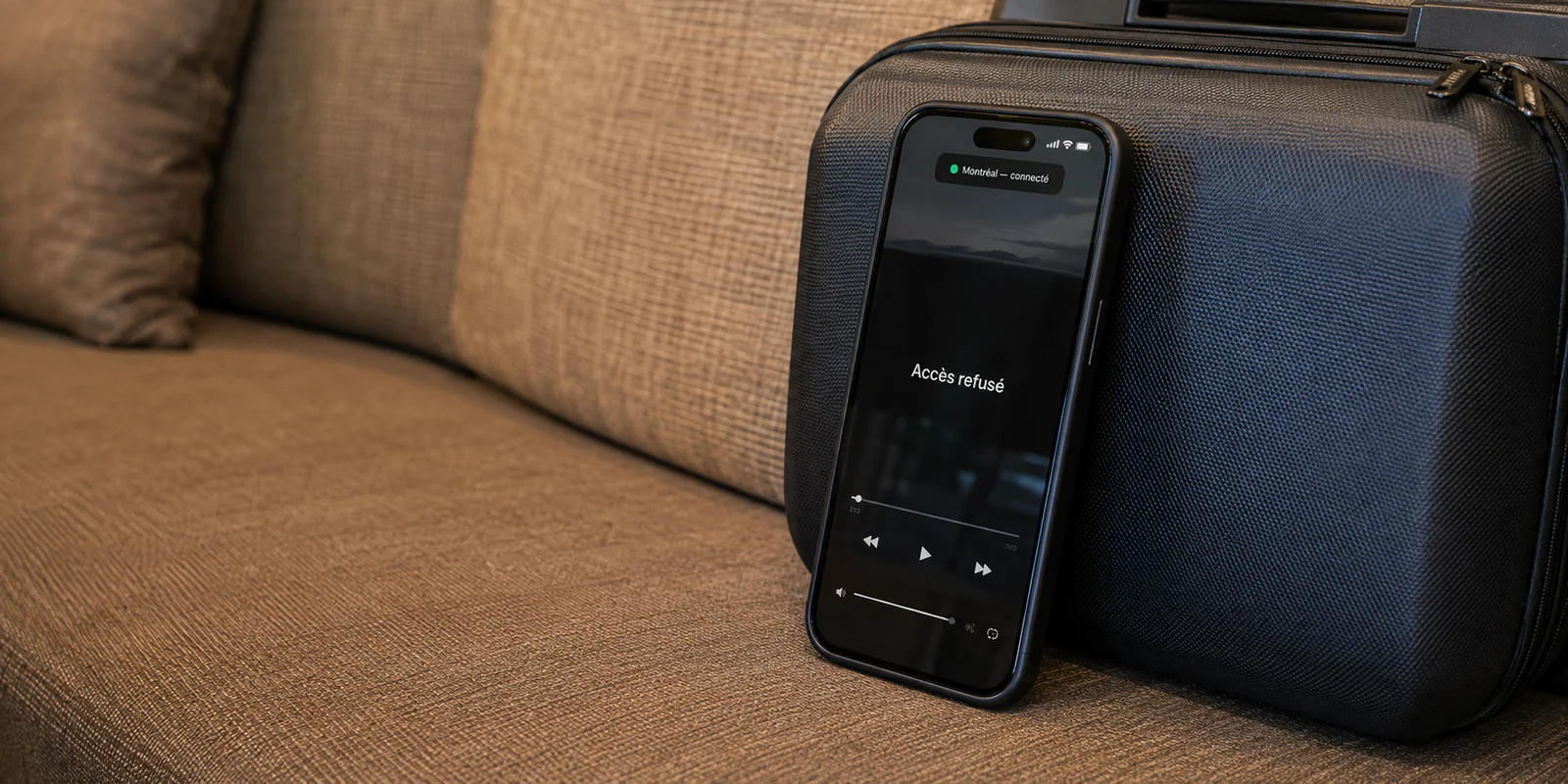 Téléphone affichant une connexion VPN à Montréal et un accès refusé, posé contre une petite valise dans un salon d’hôtel