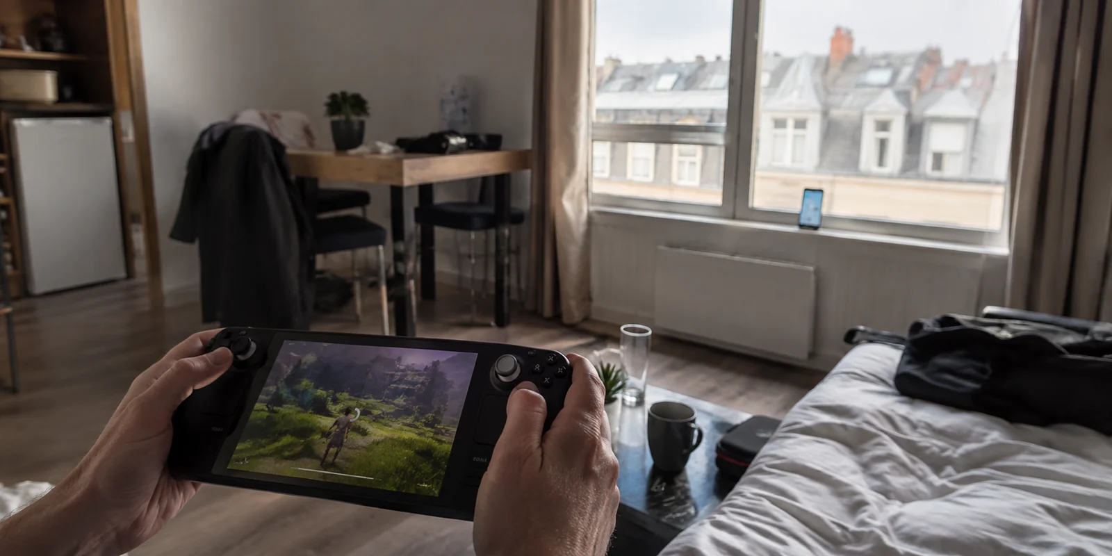 Console portable connectée au partage 5G d’un téléphone placé près de la fenêtre dans un appartement de location