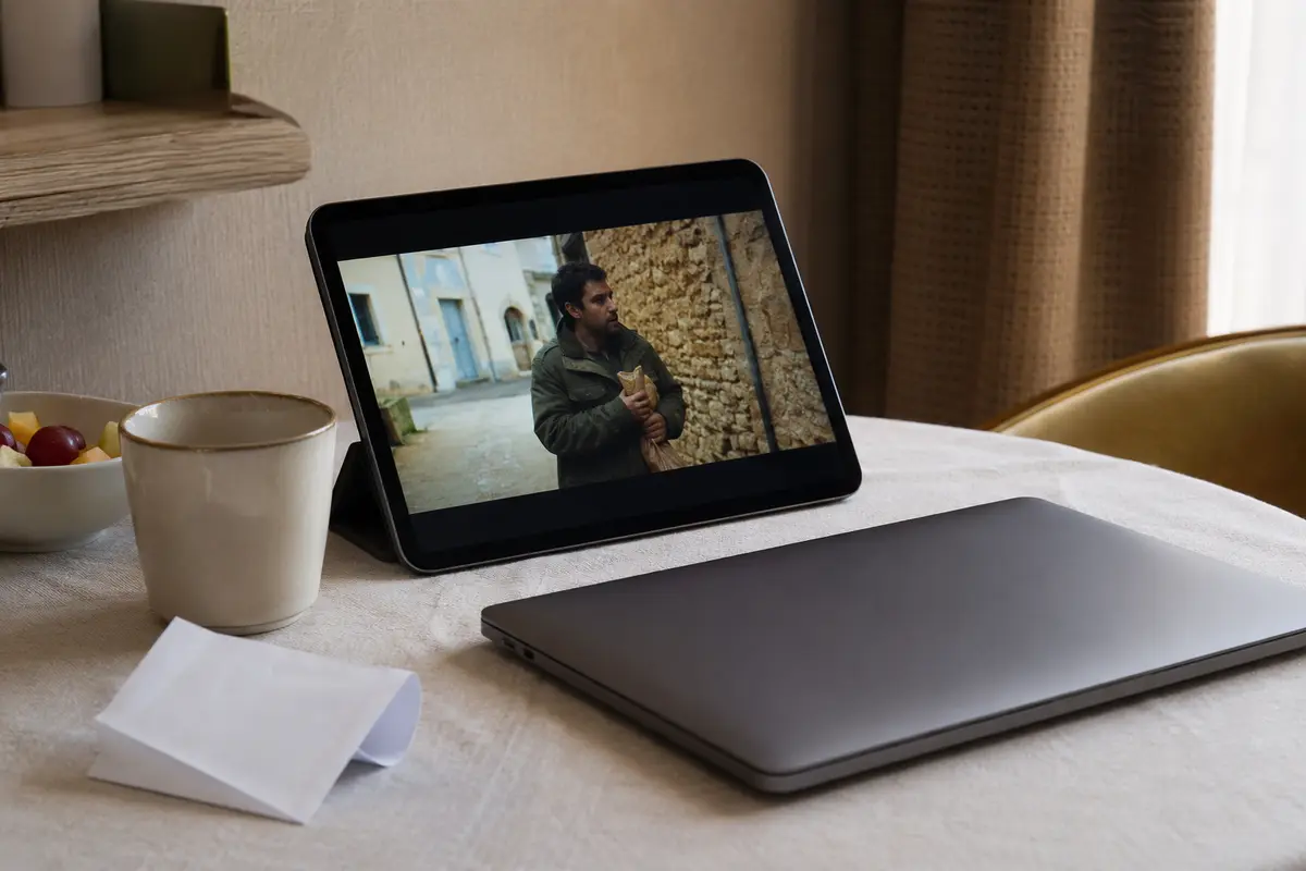Une tablette diffuse un programme vidéo sur une table de petit-déjeuner à côté d’un ordinateur fermé