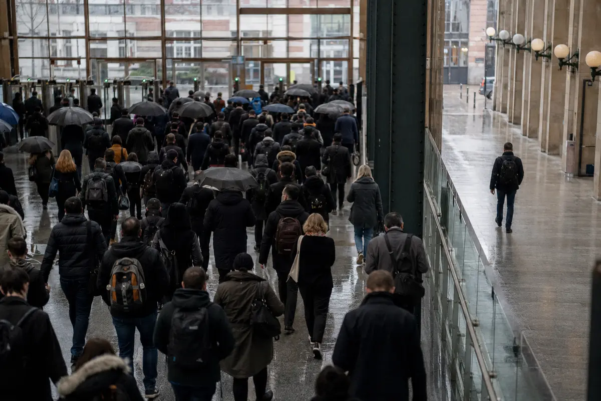 Une foule de voyageurs emprunte une sortie de gare tandis qu’une personne marche seule dans un passage voisin