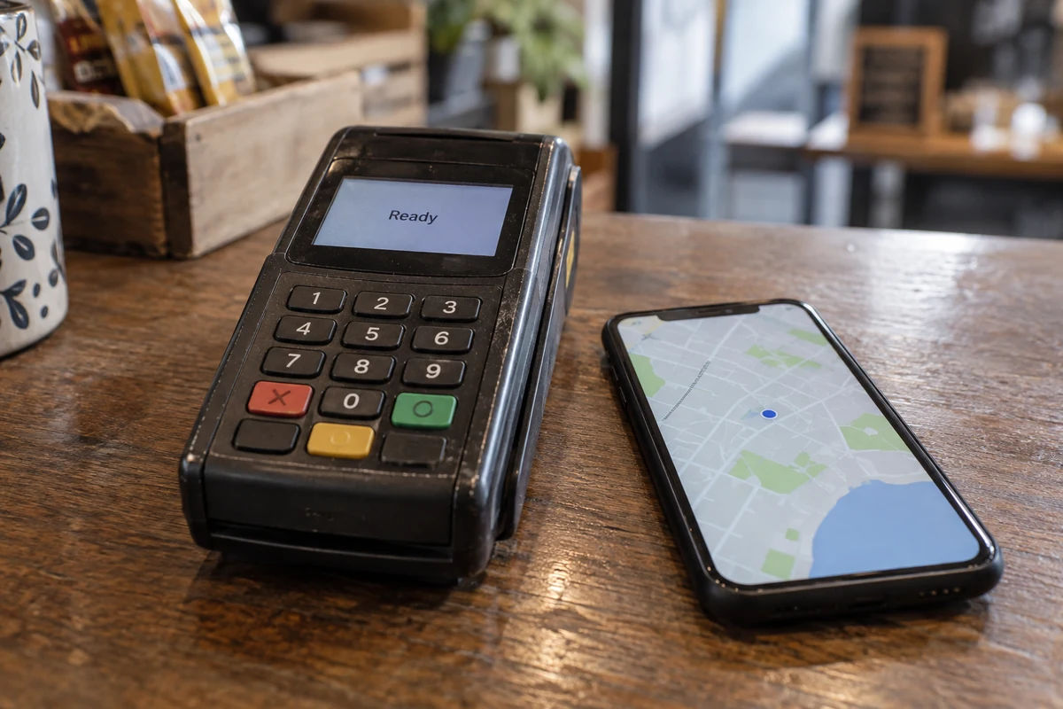 A merchant card terminal beside a phone displaying its map location.