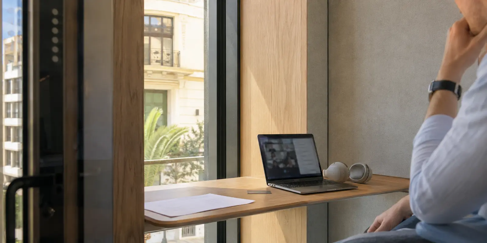 Área de reuniones de un coworking en Valencia con un portátil en videollamada, auriculares, agenda y una tarjeta bancaria sobre la mesa