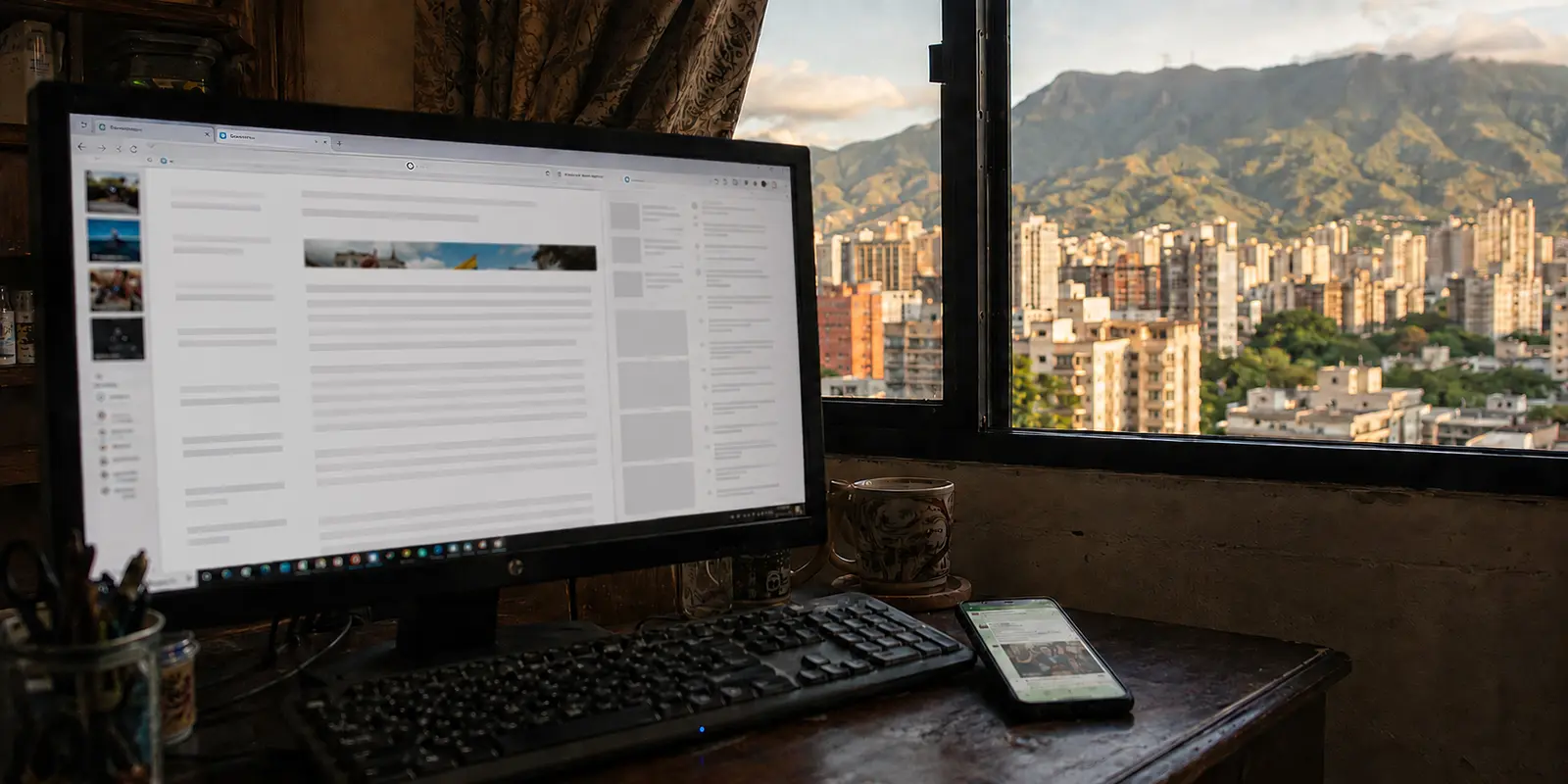 Página de noticias detenida durante la carga en un monitor frente a una ventana con vista de Caracas y el Ávila