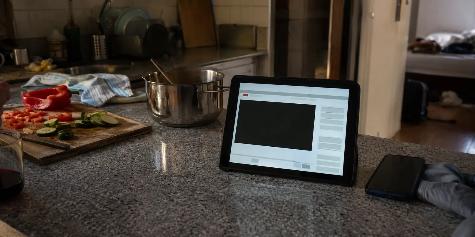 Una tableta en la cocina de un alojamiento muestra un reproductor de televisión española que no arranca, junto a un móvil usado como hotspot