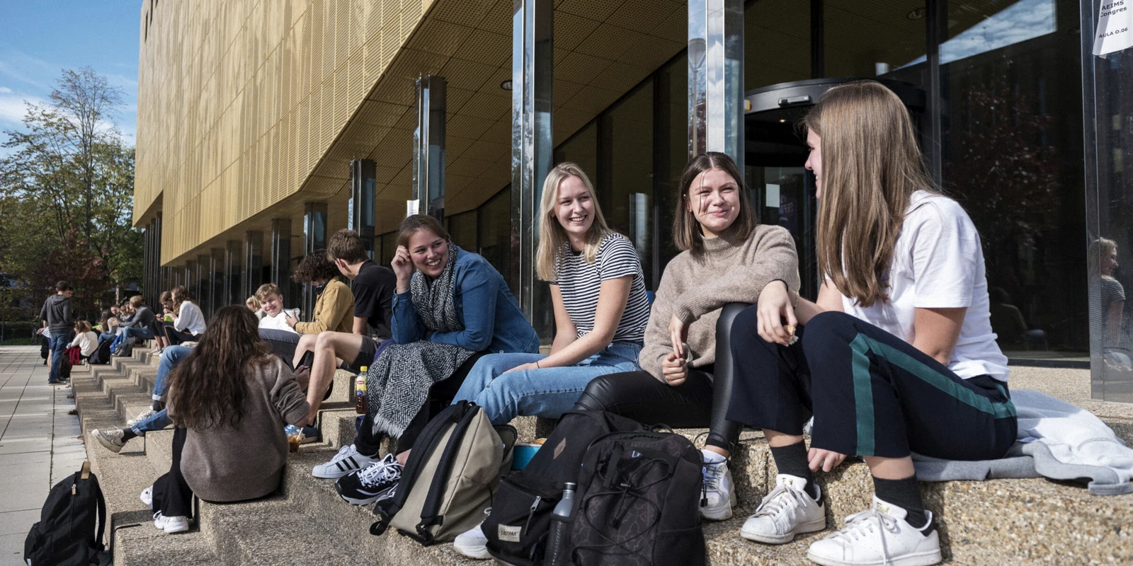 Travelers sitting with backpacks outside a modern public building before a trip.