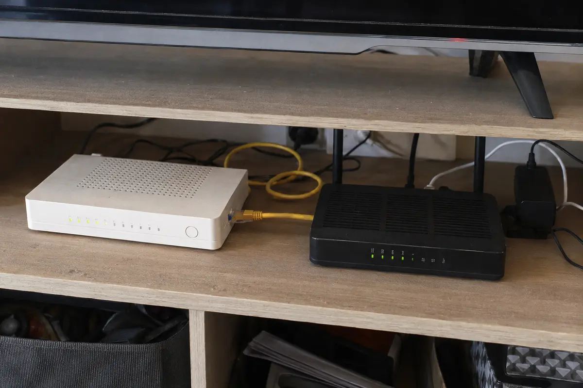 Une box fibre reliée à un second routeur et à plusieurs alimentations dans un meuble TV