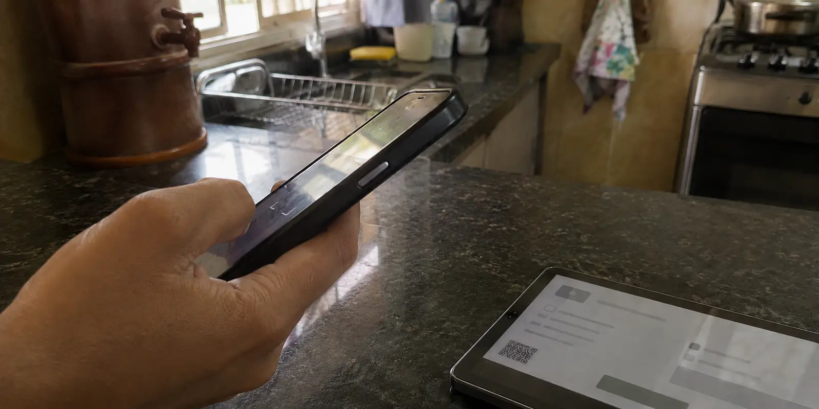 Celular sendo usado para escanear um pagamento por QR Code em um tablet sobre a bancada da cozinha
