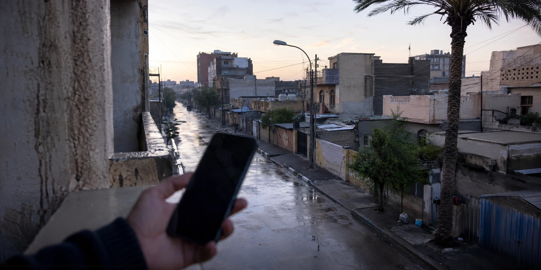 شارع سكني مبلل في مدينة عراقية وهاتف في المقدمة